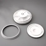 Tapa plástica blanca y aro de silicona para contenedor de vidrio, con piezas desmontadas sobre fondo gris