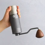 Mano sosteniendo Molinillo Manual de Café Sweenuts Pro gris con manivela y pomo de madera